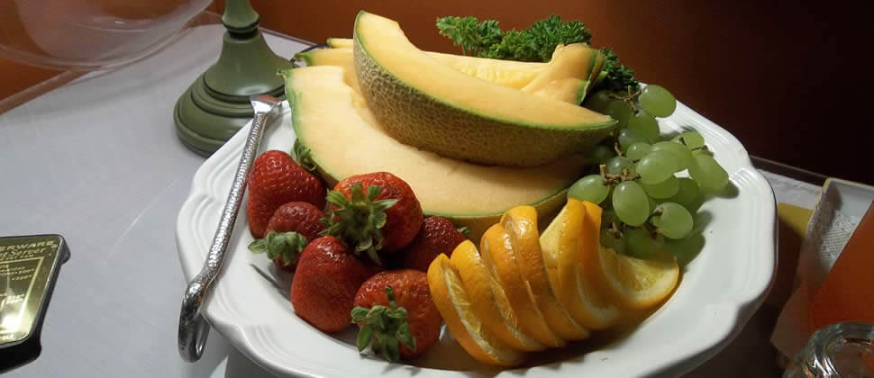 A colorful plate of fruit, including red strawberries, oranges and green grapes on a white plate