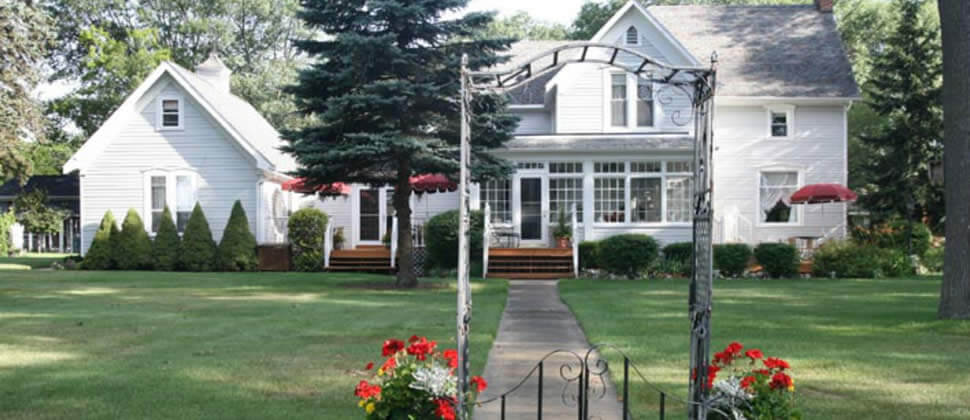 view of the white clapboard inn from the street, view of the lawn and inn through an iron gate and archway