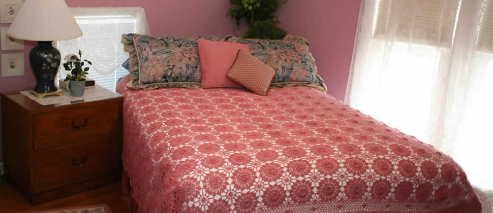 guestroom with rose colored walls, natrual sunllight through white sheers, intricate crochet rose colored bedspread