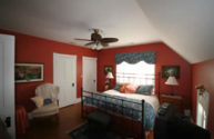 guest room with red painted walls, ceiling fan, black iron bed with blue floral window treatment and bed linens 