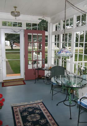 glass enclosed porch with red door, light hanging above glass and iron rod table and two chairs