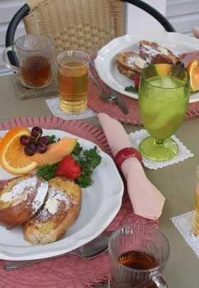 french toast and fruit medley on rose-colored place mat, coffee and apple juice in clear glasses, and tinted green glass 