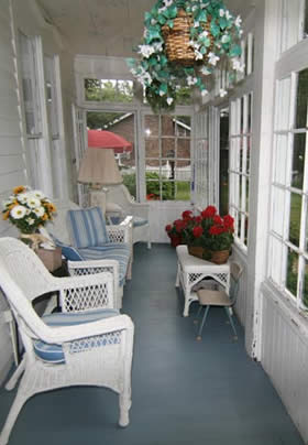 View of porch, white wicket chair, hanging plant, redd flowers